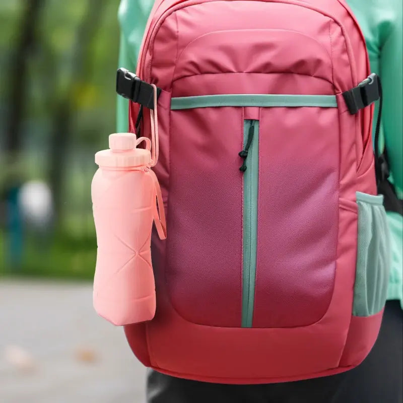 Pink folding water cup attached to a red backpack, perfect for outdoor adventures.