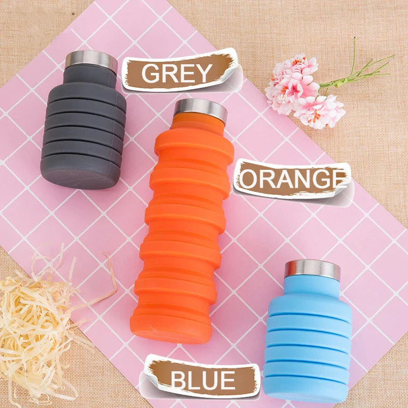 Collapsible water bottle in grey, orange, and blue colors on a pink checkered background.